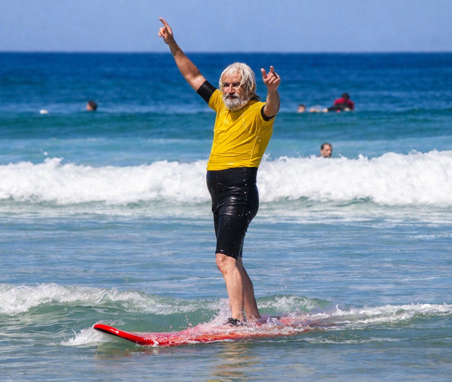 Surfeur senior les bras levés sur la plage face à l’océan