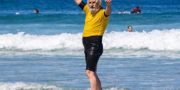 Surfeur senior les bras levés sur la plage face à l’océan